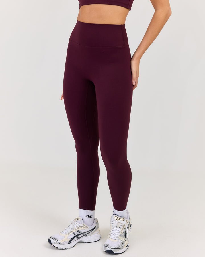 Person wearing maroon leggings and white sneakers on a light gray background