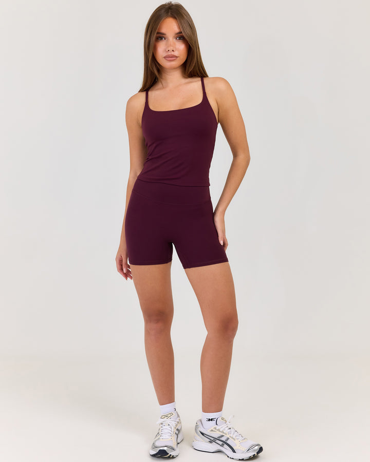 Woman wearing a maroon tank top and shorts set on a white background