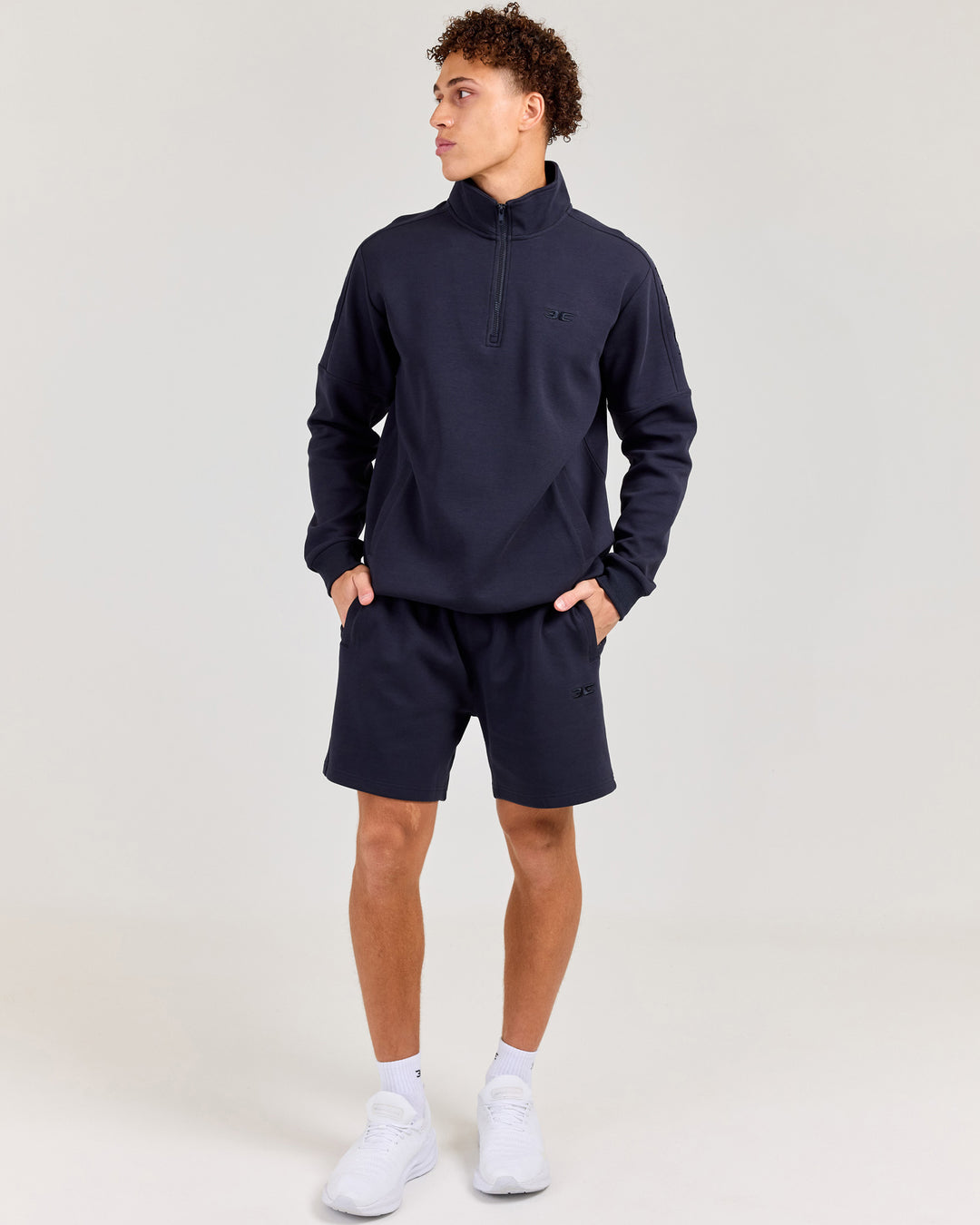 Man wearing a navy tracksuit with white sneakers on a light gray background