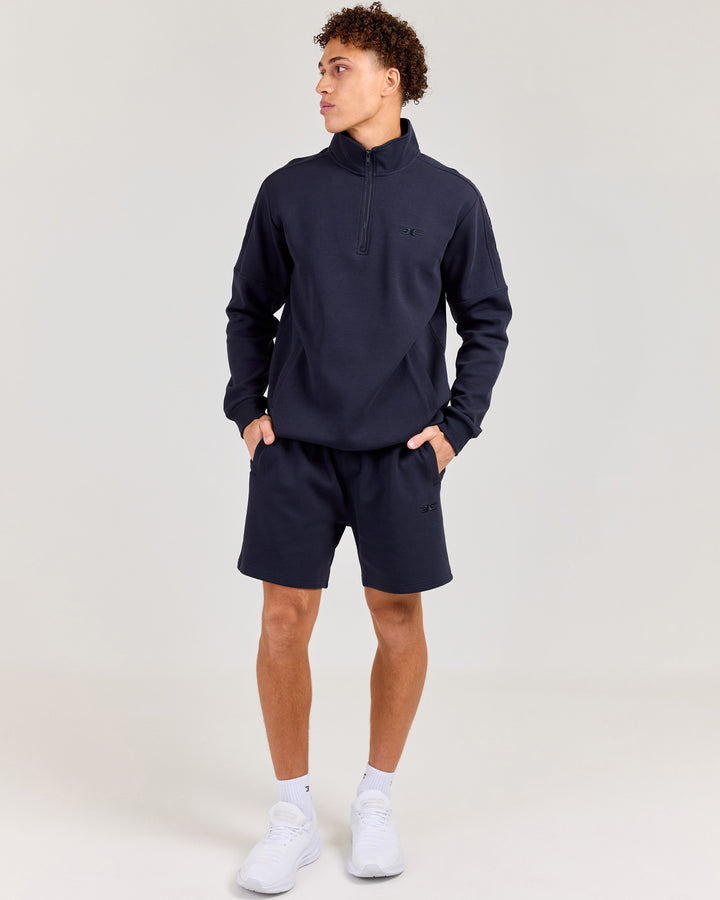 Man wearing a navy tracksuit with white sneakers on a light gray background